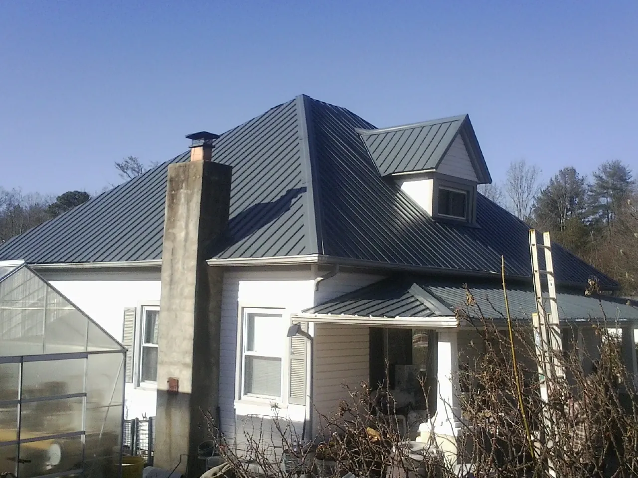 Dark blue standing seam metal roof on a white farmhouse with dormer — Slate & Tile Roof Repair by Roofing Brothers in Corry