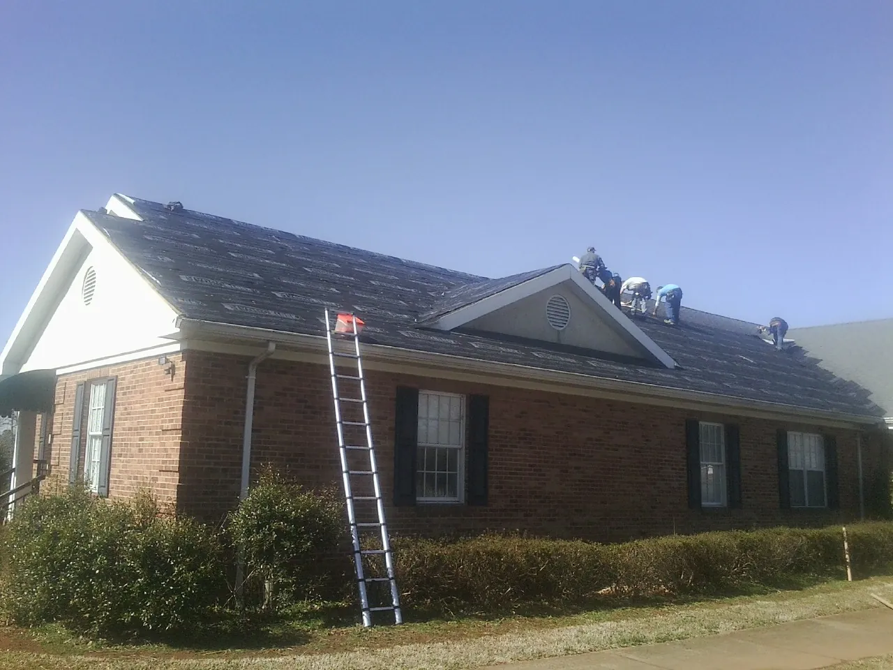 Crew tearing shingles off a brick ranch roof with a ladder set — Metal Roof Repair work by our crew in Corry
