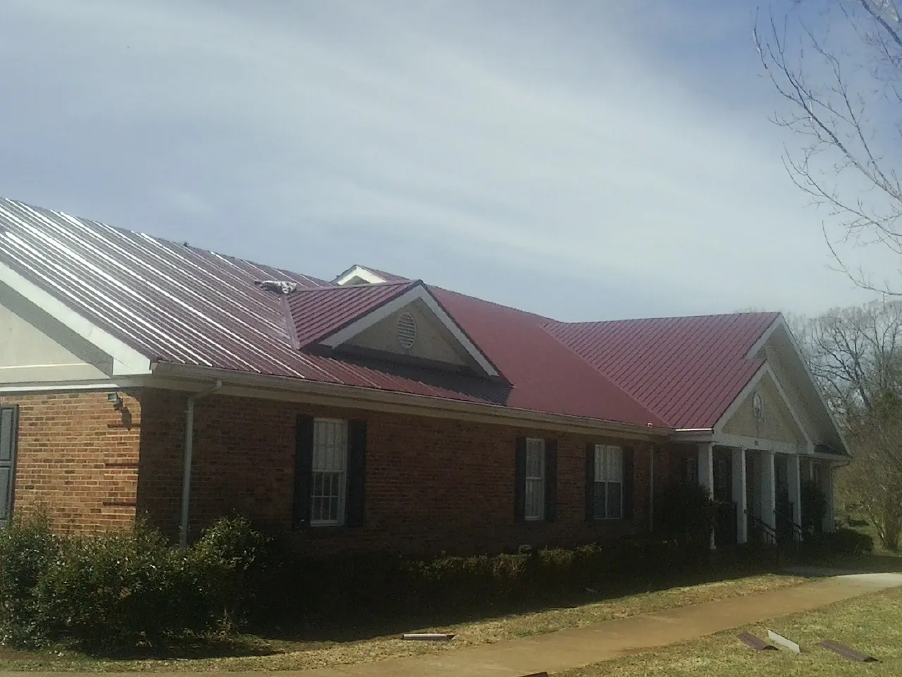 Red metal roof with gabled entries on a long brick building, from a Hail Damage Roof Repair job in Corry