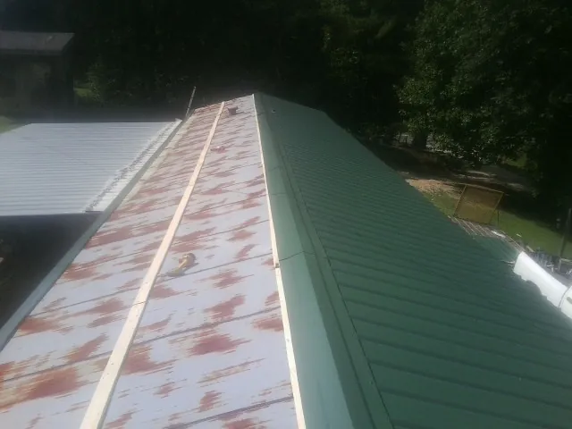 Old rusted panels beside newly installed green metal roofing — Wind Damage Roof Repair by Roofing Brothers in Corry
