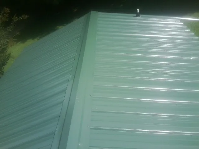 New green metal panels meeting at the ridge of a roof — Flat Roof Repair work by our crew in Corry