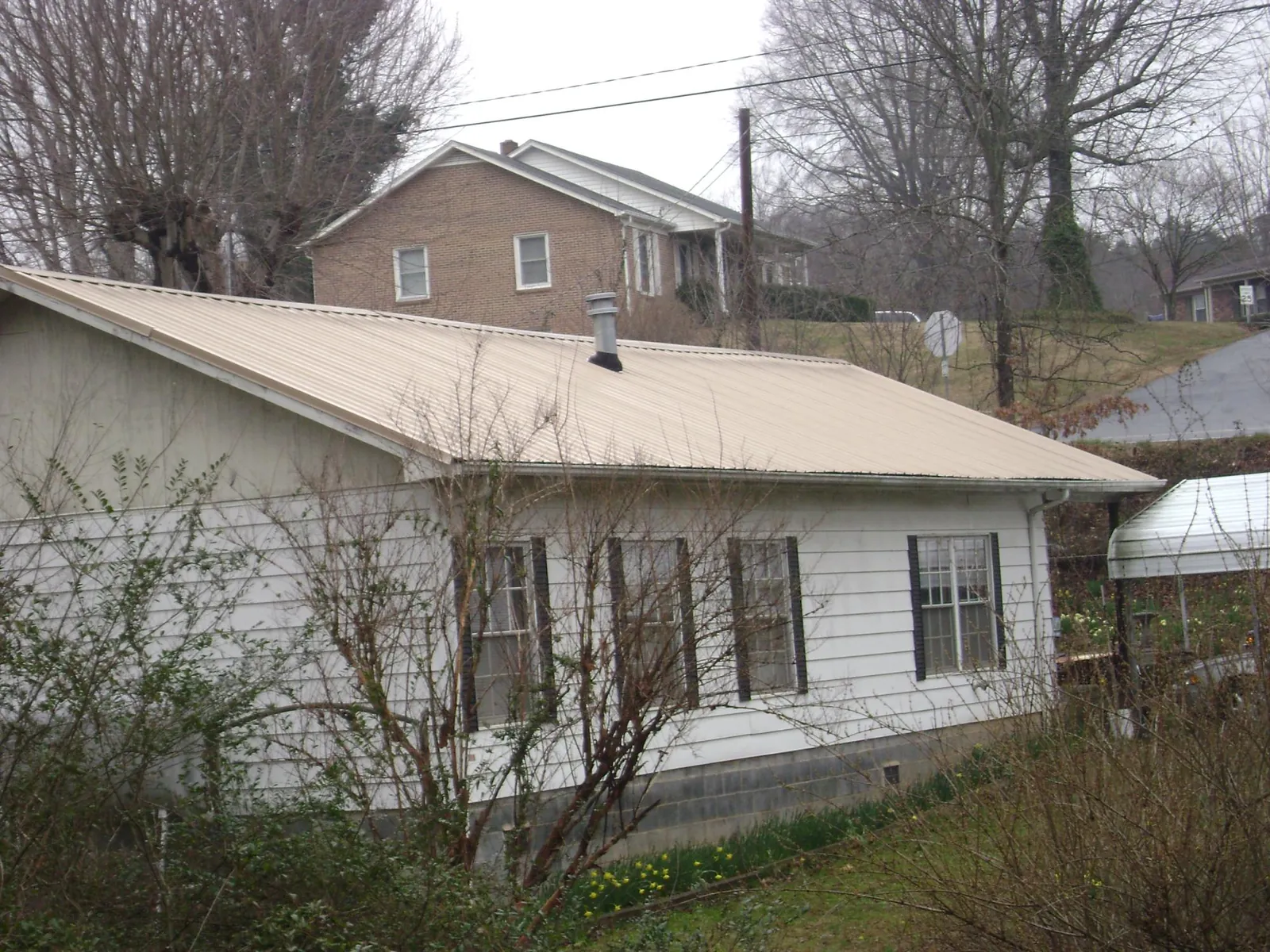 Tan metal roof on a white sided house set into a hillside — Commercial Roofing by Roofing Brothers in Corry