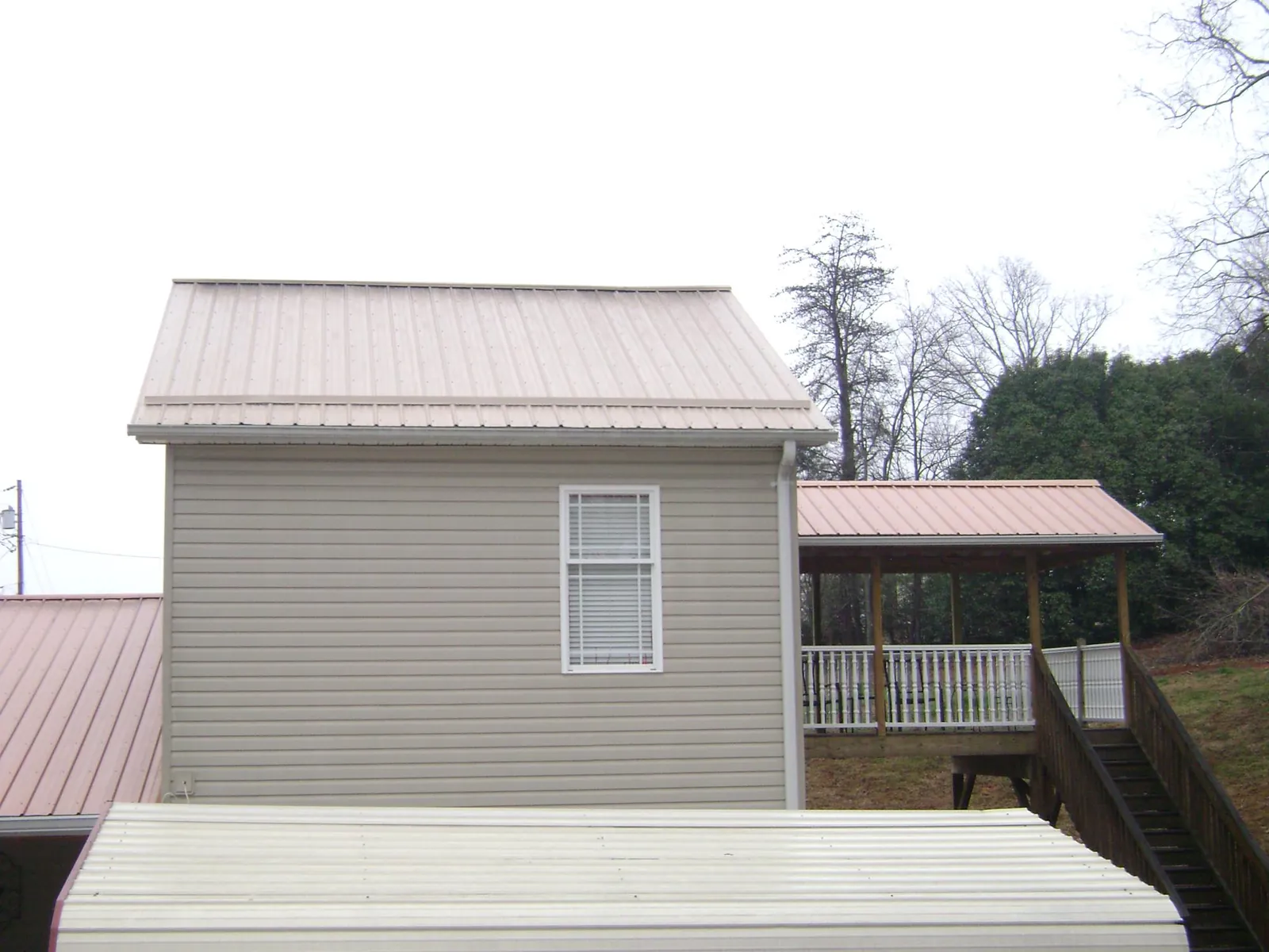 Tan metal roofs on a two story addition and attached porch, from a Roof Replacement job in Corry