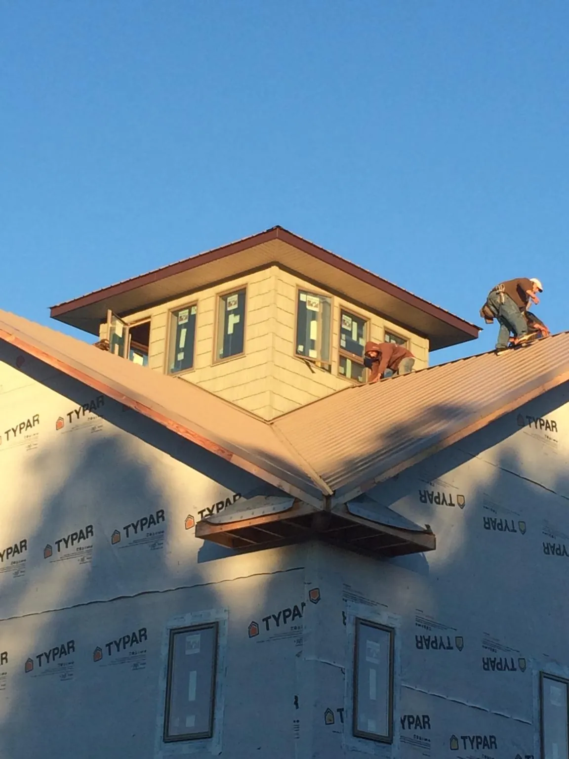 Roofers working around a rooftop cupola on a new metal roof at sunset — Roof Waterproofing in Corry by Roofing Brothers